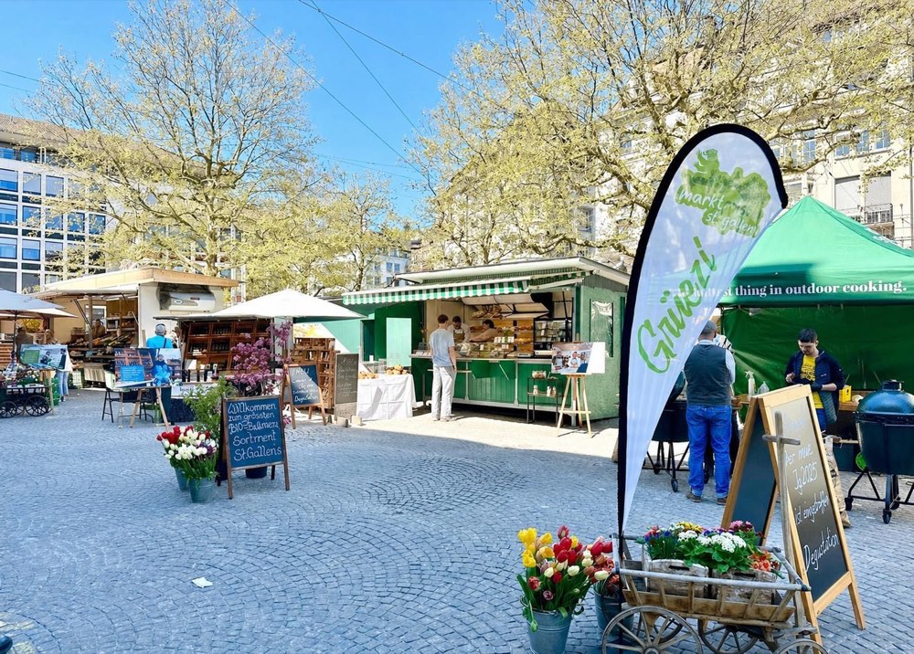 Der Marktplatz St. Gallen im Frühling mit Marktständen, Bäumen und Blumen