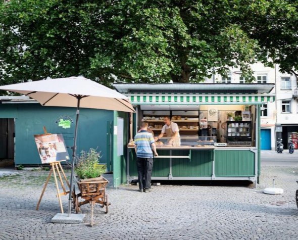 Der grüne Marktstand unter grossen Bäumen, ein Kunde wird bedient